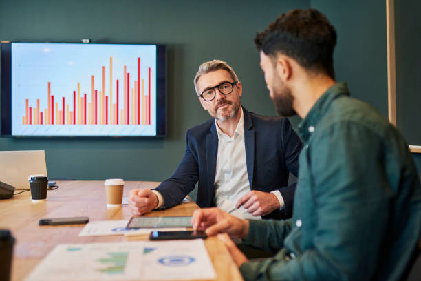 des professionnels confiants engagés dans une discussion sérieuse sur des questions importantes dans un environnement de bureau moderne - augmenter vos revenus photos et images de collection
